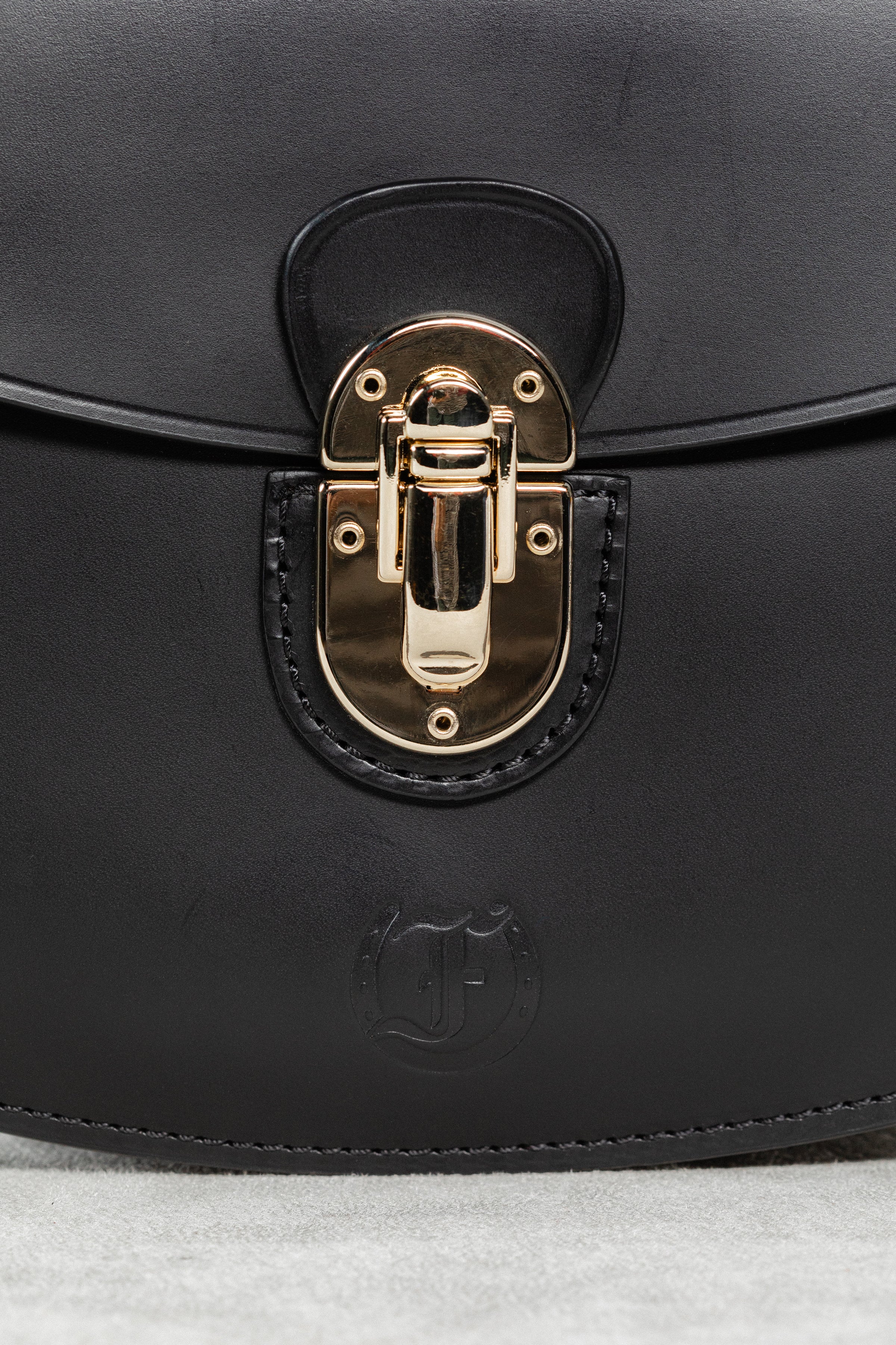 Close-up of black leather Minibus Bag by Freedman's, highlighting gold-tone turn-lock closure and embossed brand logo.