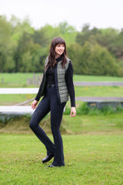 Ladies Essential Quilted Vest by Freedman's in Military Green with Black side accent and black zipper detail, modeled by smiling woman with dark long hair wearing slate black top and black jods against natural background, showing athletic apparel fit and style