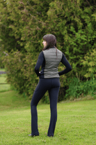 Ladies Essential Quilted Vest by Freedman's in Military Green with Black side accent and black zipper detail – Back View, modeled by smiling woman with dark long hair wearing slate black top and black jods against natural background, showing athletic apparel fit and style