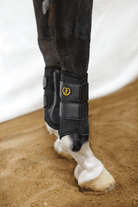 Horse wearing black splint boots for leg protection and support during training.