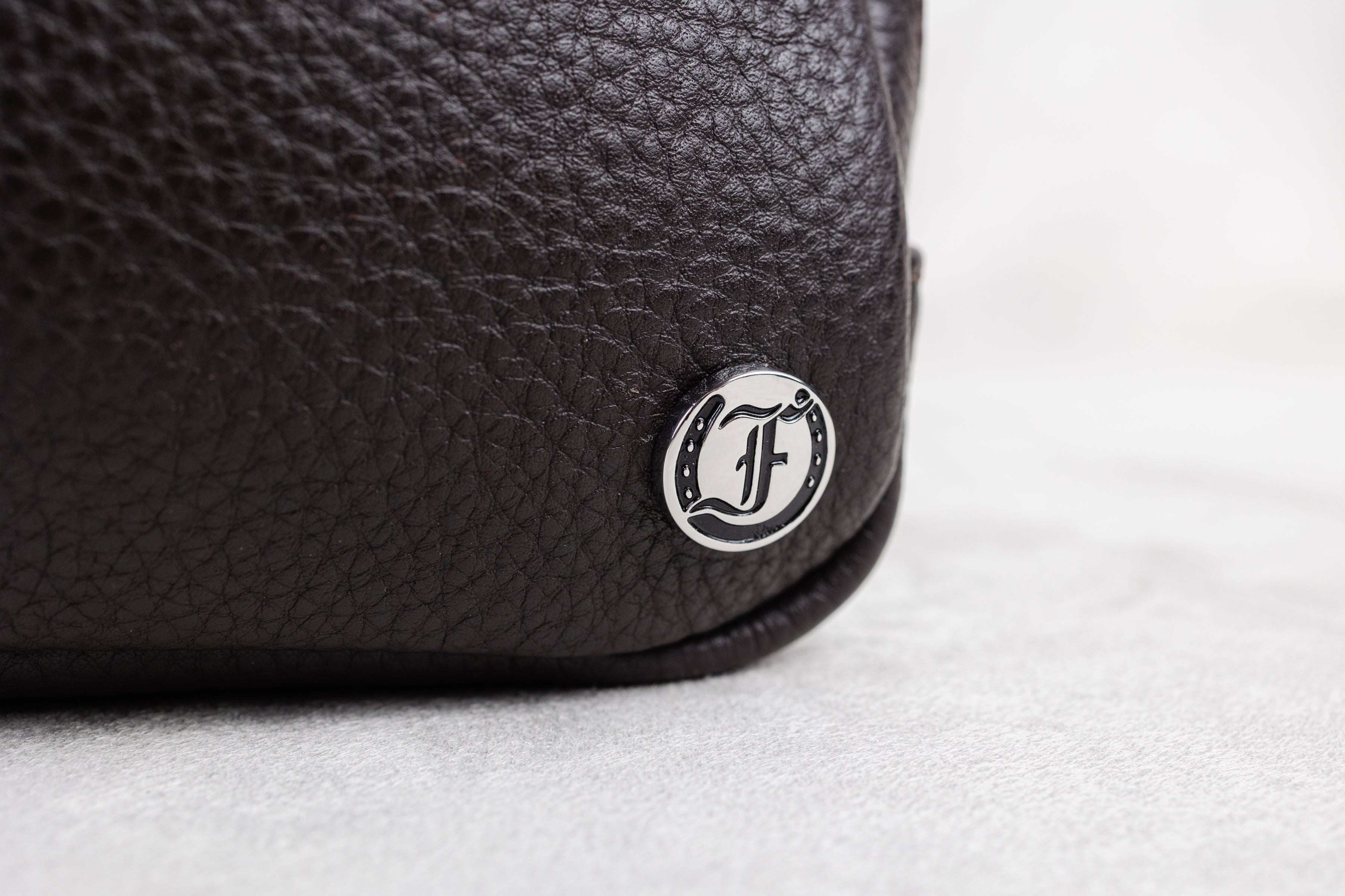 Close-up of a brown leather bag with a brand logo on a light background