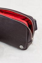 Brown leather crossbody or waist bag with unzipped with red lining interior showing  on white background