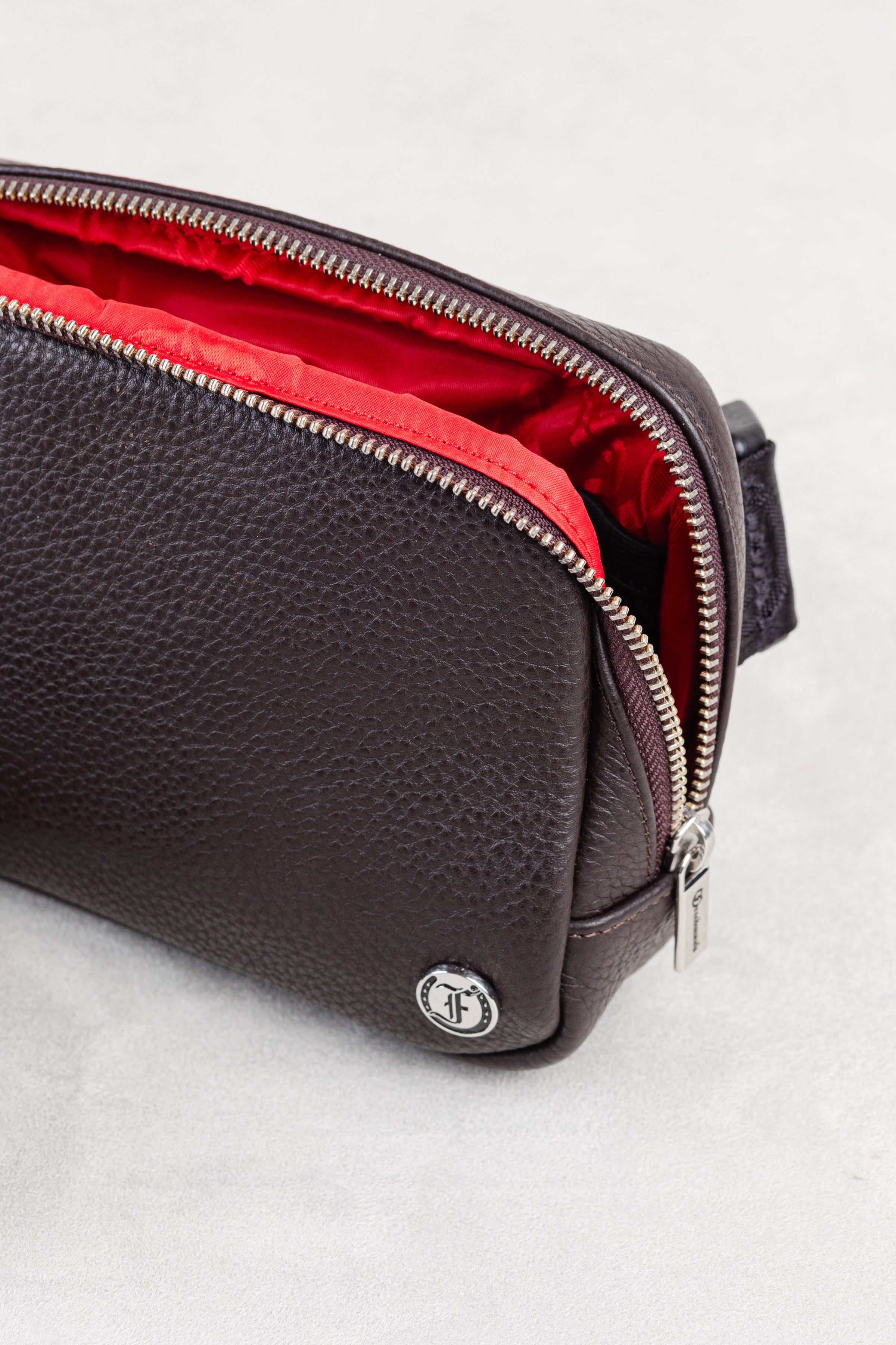 Brown leather crossbody or waist bag with unzipped with red lining interior showing  on white background