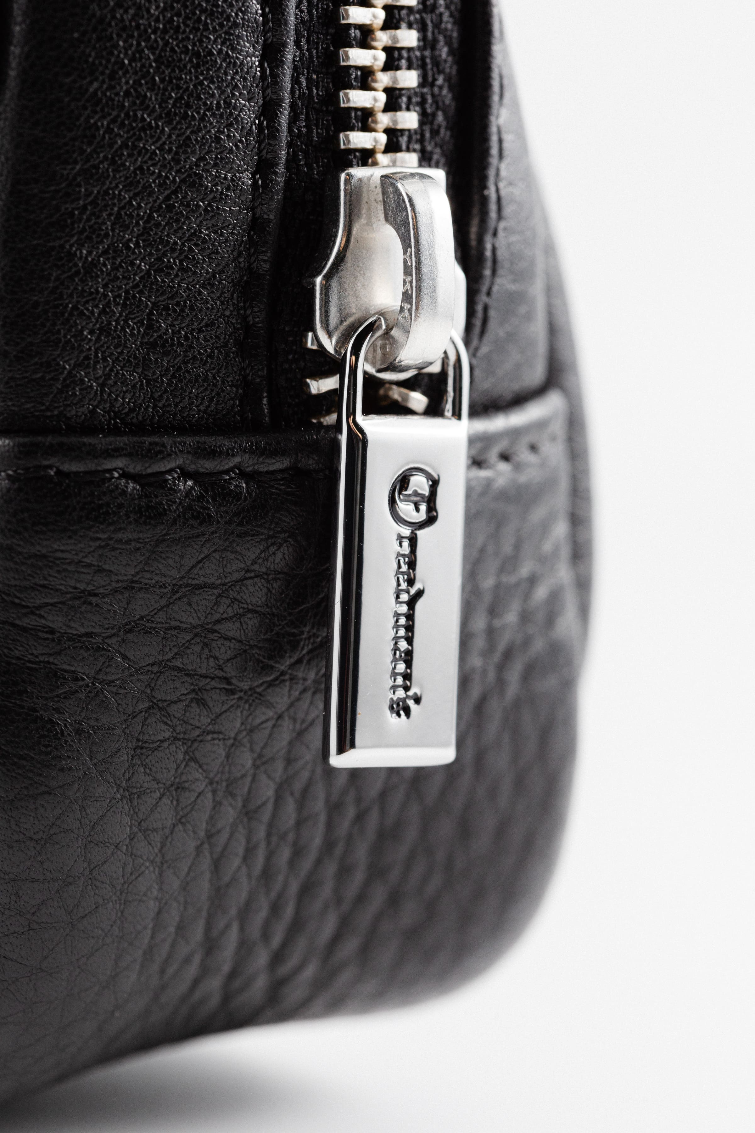 Extreme close-up of Freedman's Norfolk Crossbody Bag in Black Leather, showing silver zipper pull with engraved Freedman's logo.