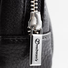 Extreme close-up of Freedman's Norfolk Crossbody Bag in Black Leather, showing silver zipper pull with engraved Freedman's logo.