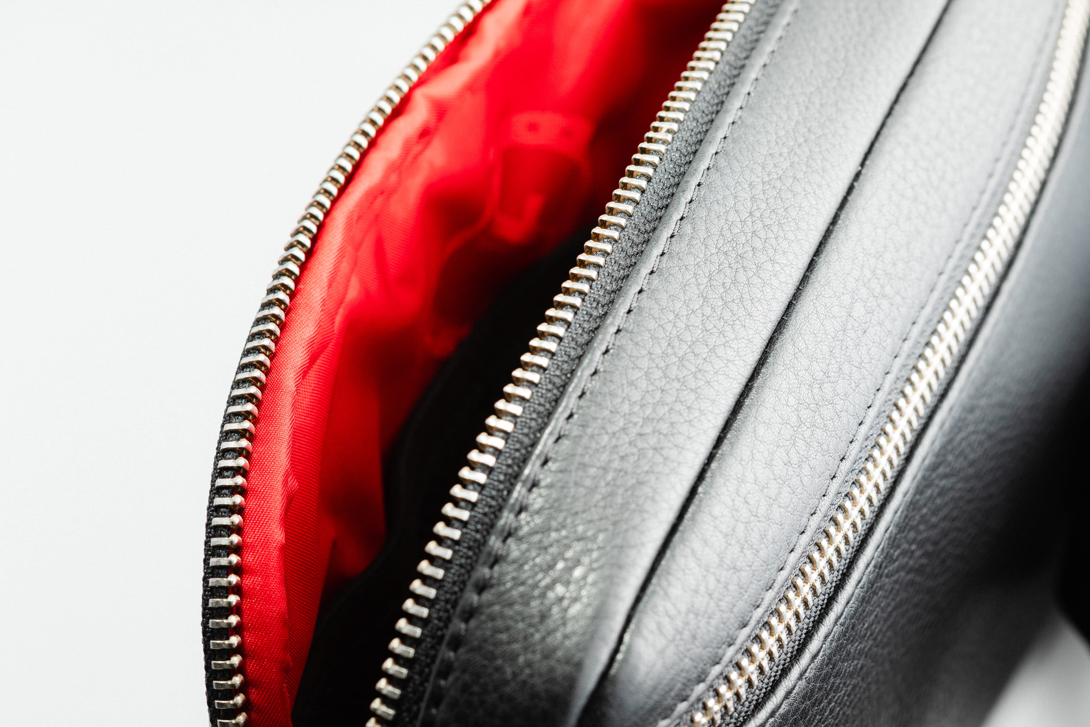 Close-up of Freedman's Norfolk Crossbody Bag in Black Leather, showing red interior lining and silver zipper.