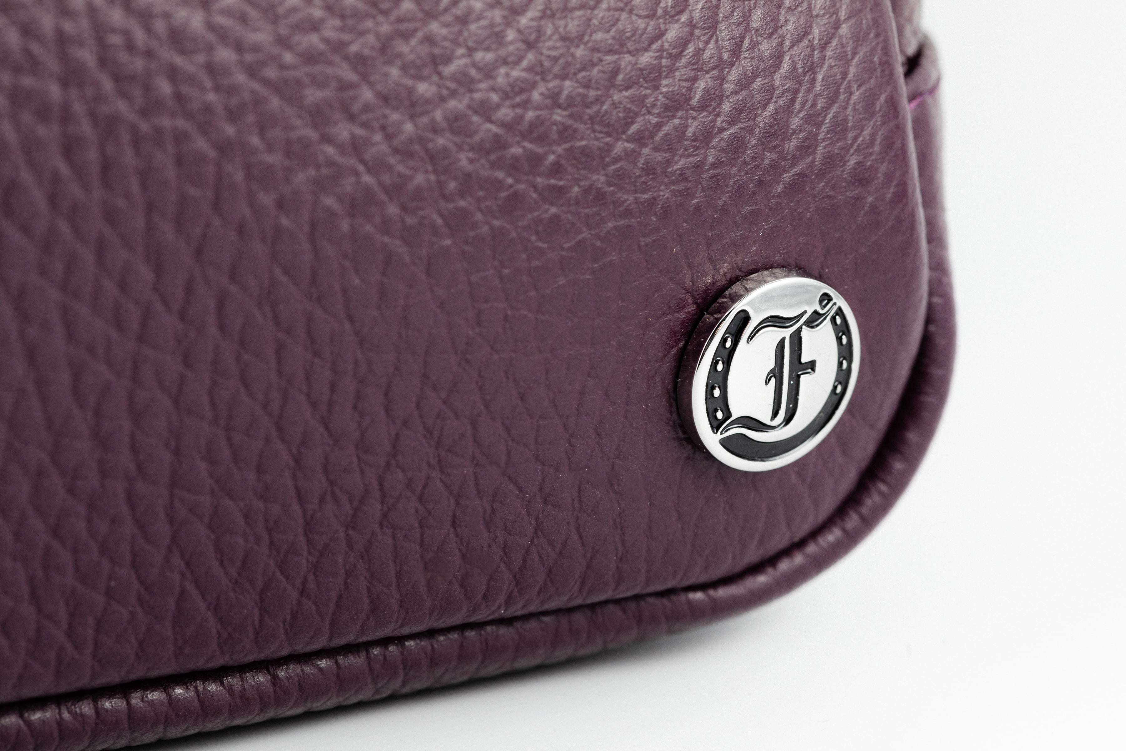 Close-up of Freedman's Norfolk Crossbody Bag in Purple Leather, showing silver logo medallion on textured leather.