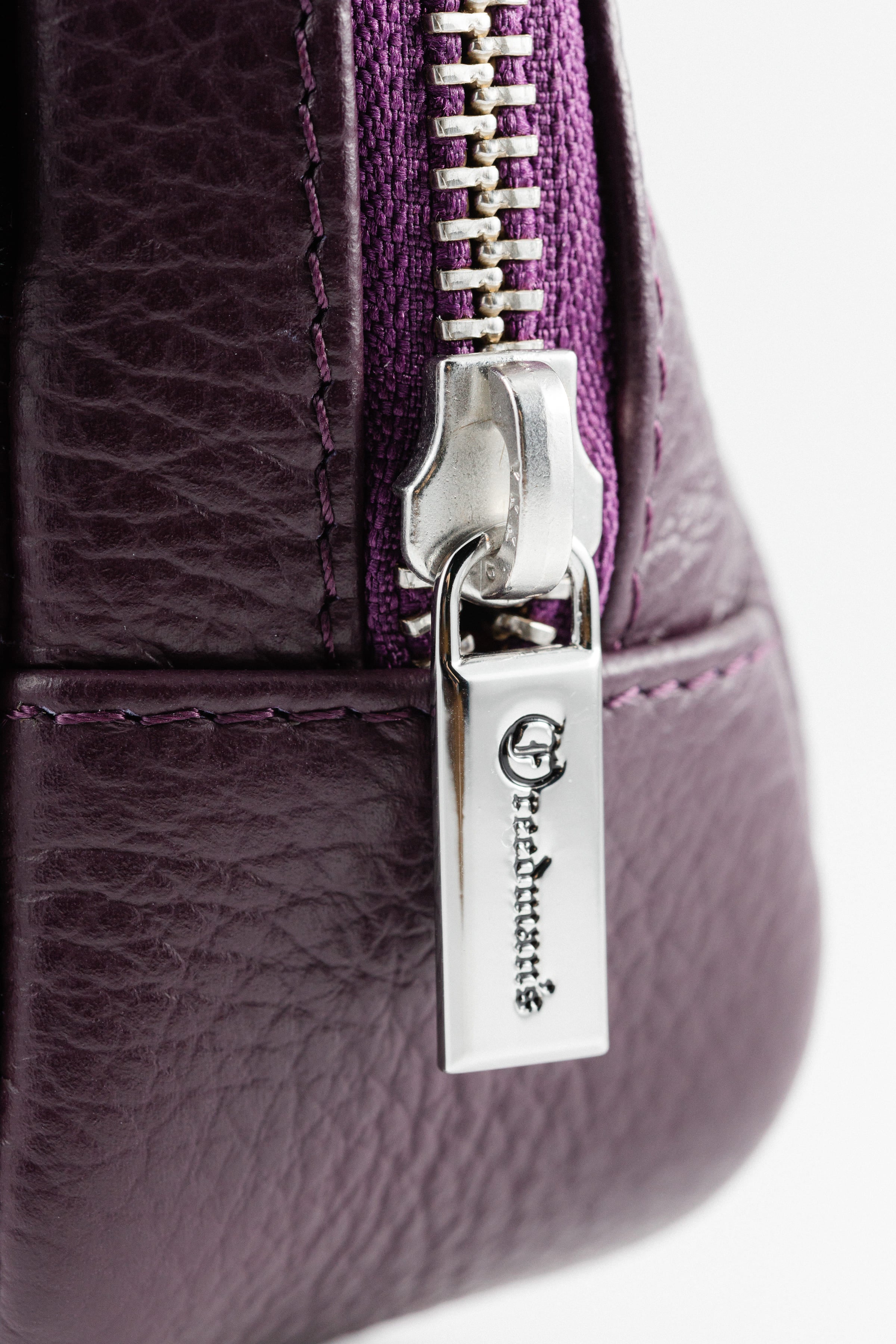 Extreme close-up of Freedman's Norfolk Crossbody Bag in Purple Leather, showing silver zipper pull with engraved "Freedman's" logo.