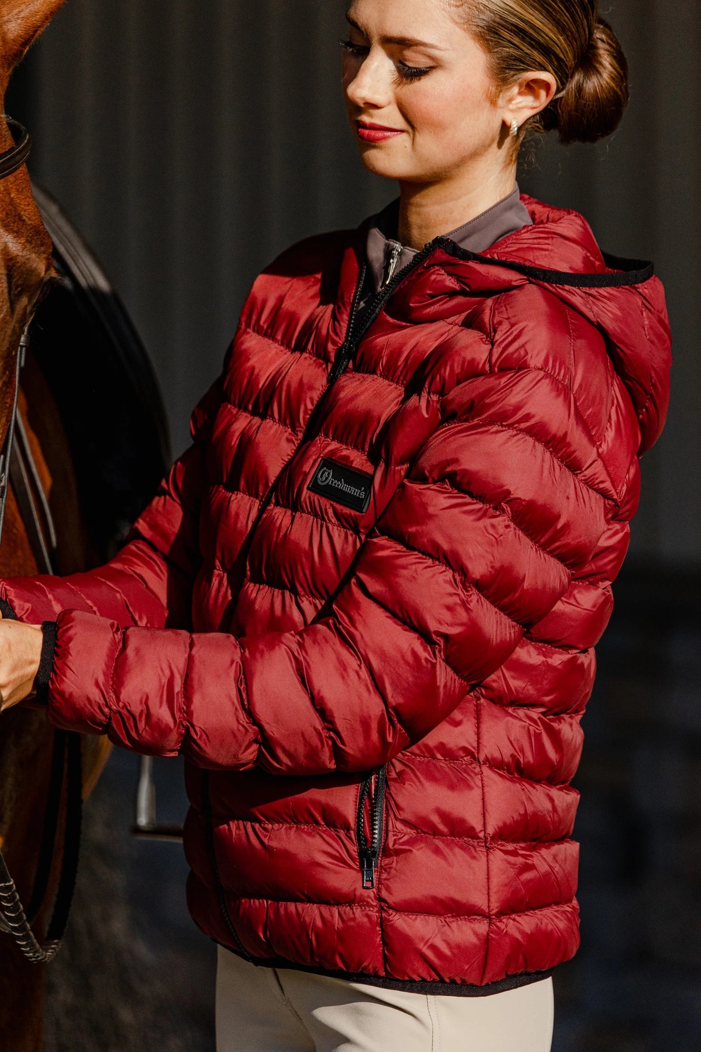 Woman wearing the Signature Ladies' Packable Puffer Jacket in burgundy, highlighting the quilted design, hood, front zipper, and zippered pockets.