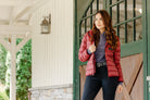 Woman wearing the Signature Ladies' Packable Puffer Jacket in burgundy, featuring a quilted design, front zipper, zippered pockets, and hood, leaning against a stable door.