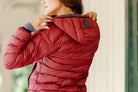 Close-up of the Signature Ladies' Packable Puffer Jacket in burgundy, highlighting the quilted back design, hood, and Freedman's logo patch.