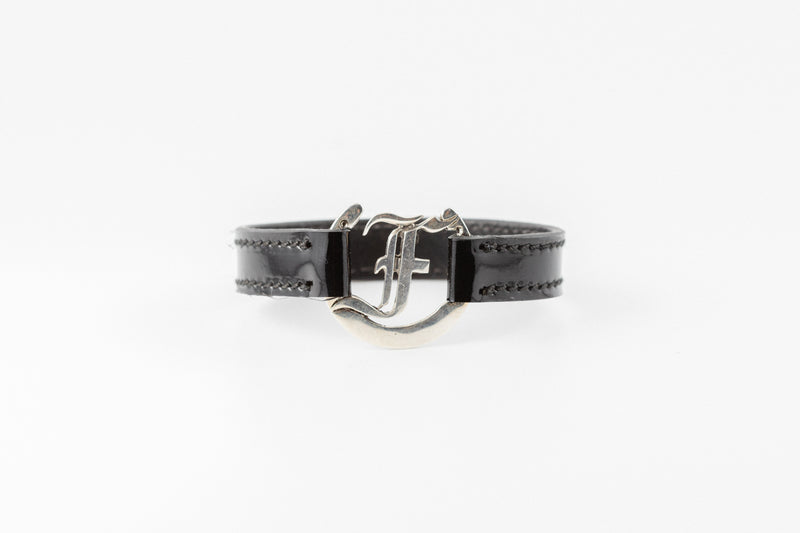 Freedman's bracelet, black patent leather band with silver F logo clasp, detailed view.