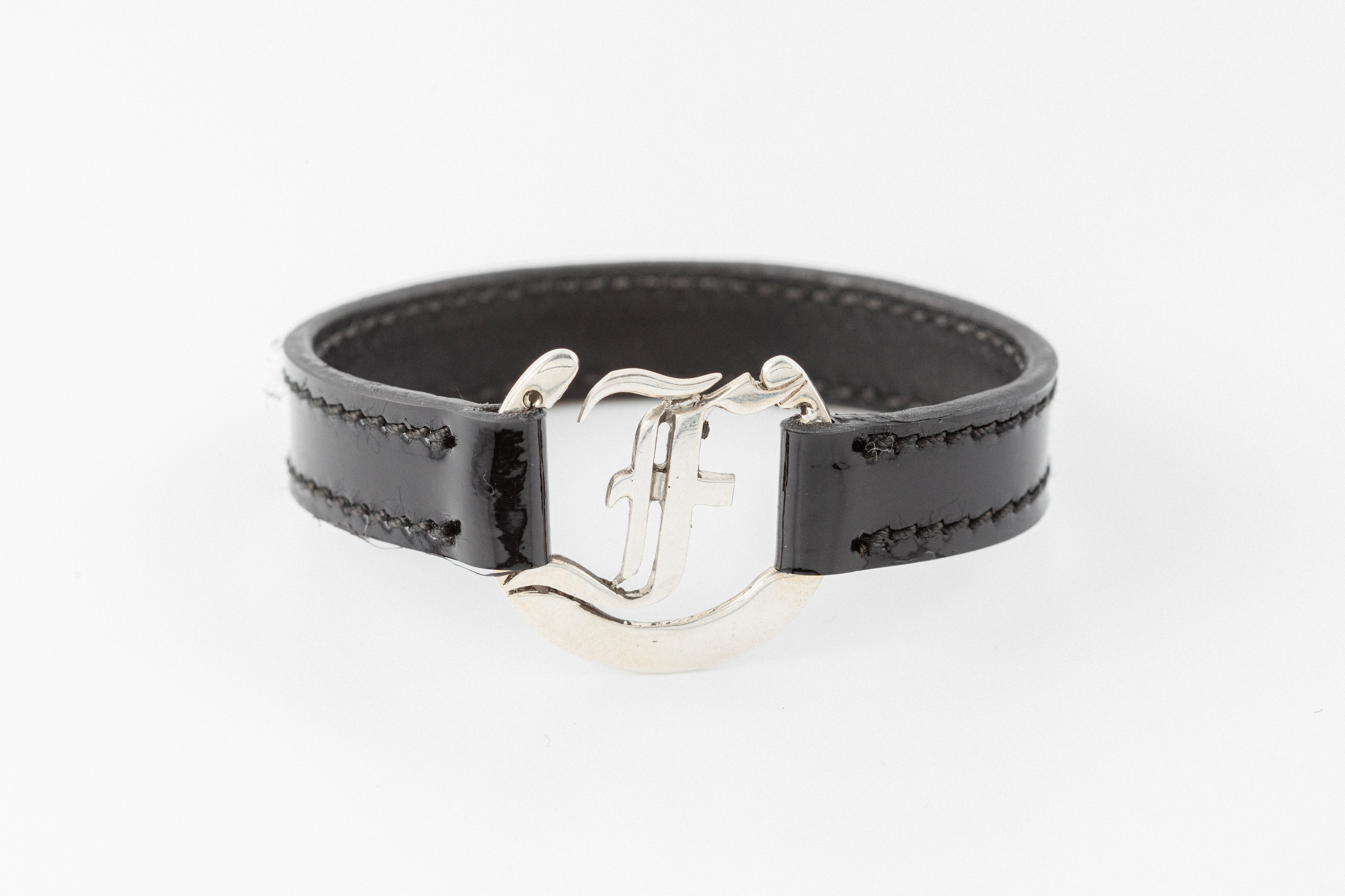 Black patent leather bracelet with silver F logo clasp, detail view by Freedman's.