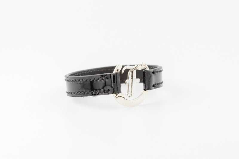 Close-up of Freedman's bracelet, showing black patent leather, sterling silver F logo, and stitching detail.