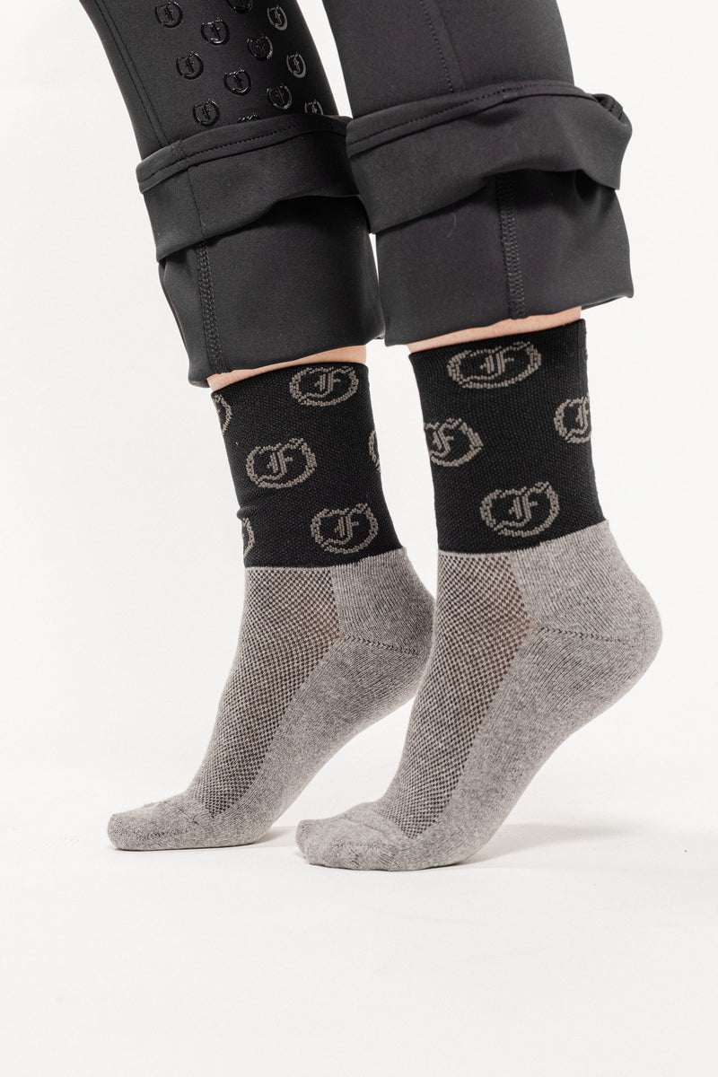 Two-tone socks, gray and black, with repeating circular Freedman's logo pattern, worn on feet,  light background.
