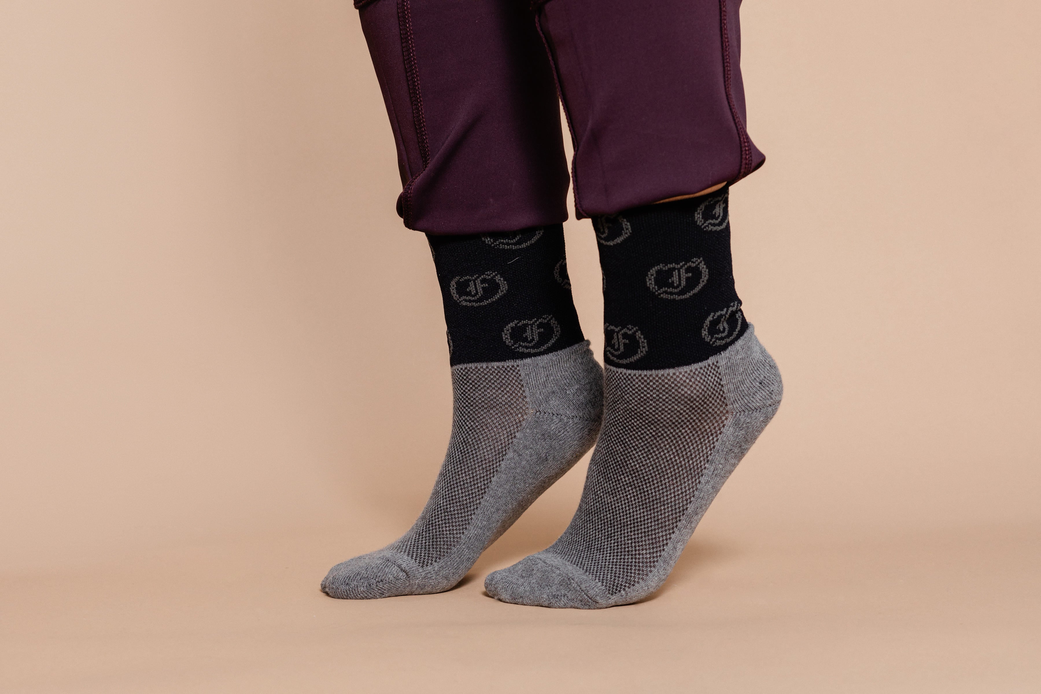 Two-tone gray and black socks with repeating circular Freedman's logo pattern, worn on feet with dark riding pants featuring visible texture and cuffs, light background.