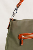  Freedman's Travois Bag in olive green, detail shot showing the silver hardware clasp, brown leather strap, and the back zipper pocket with brown leather and red zipper teeth.
