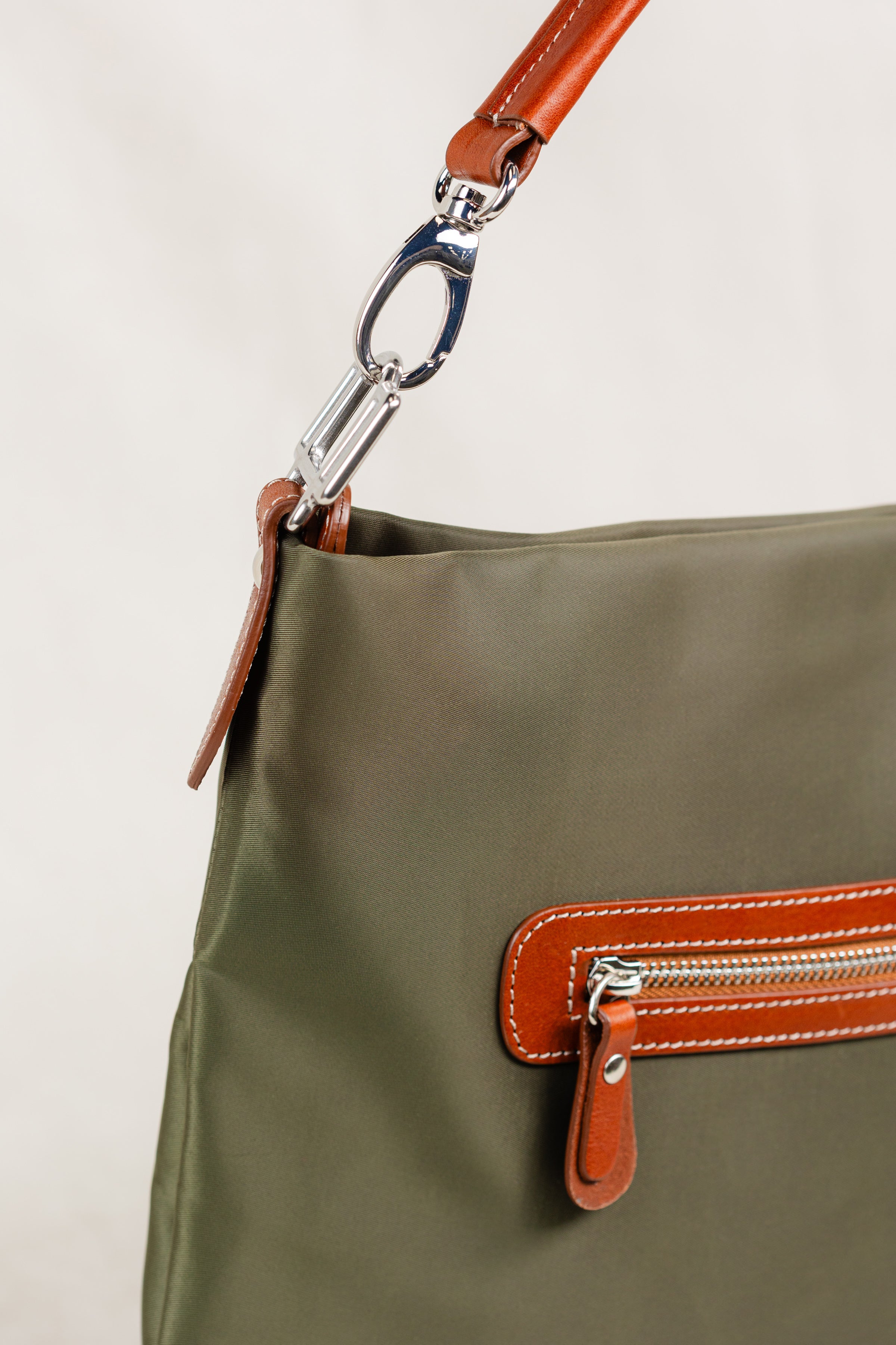  Freedman's Travois Bag in olive green, detail shot showing the silver hardware clasp, brown leather strap, and the back zipper pocket with brown leather and red zipper teeth.