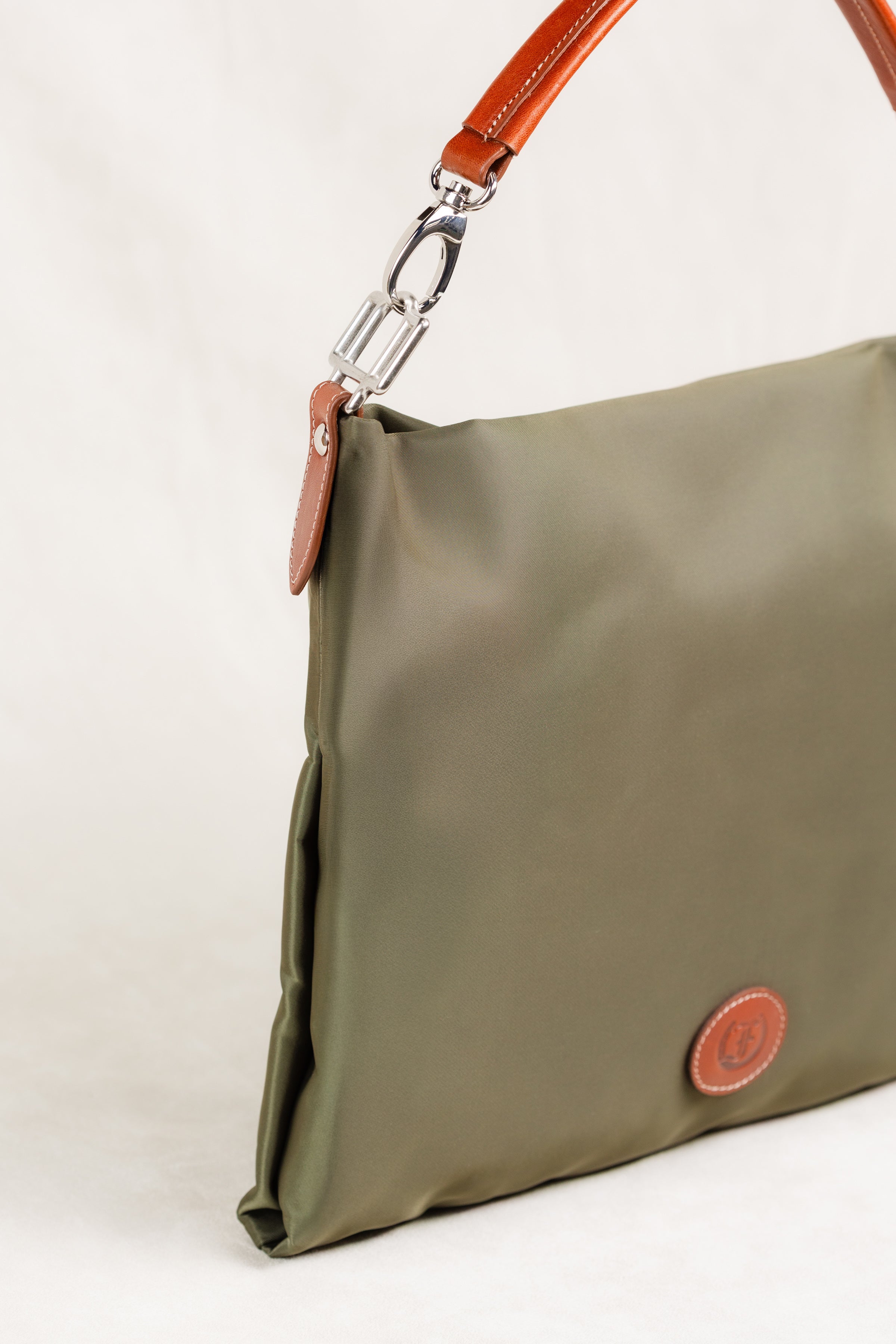 Freedman's Travois Bag in olive green, detailed side view showcasing the silver hardware connector, brown leather strap attachment, and the bag's structured side profile.
