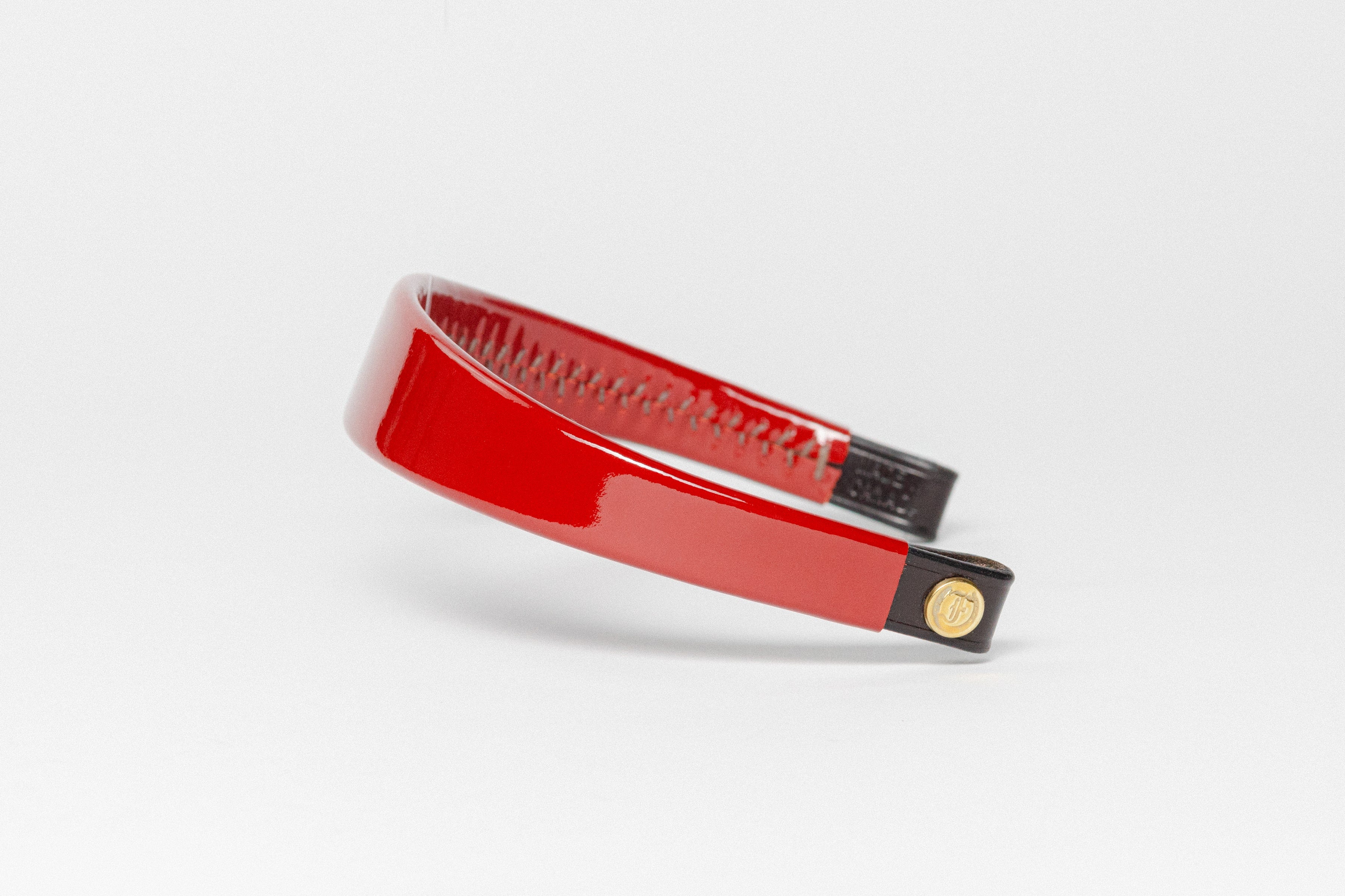 Glossy red patent leather browband, wide tapered design, dark leather ends with gold button, angled perspective.
