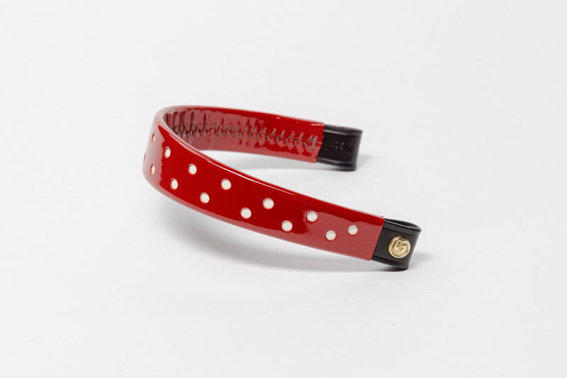 Red browband with small white dots, wide tapered design, polished brass Freedman logo buttons, and dark leather ends, angled view.