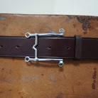 Silver bit buckle detail on brown leather belt, Weymouth model, shown on textured surface.