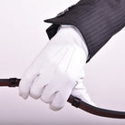 White leather show glove, The Yorkville model, worn on hand holding a riding rein, with jacket sleeve visible.