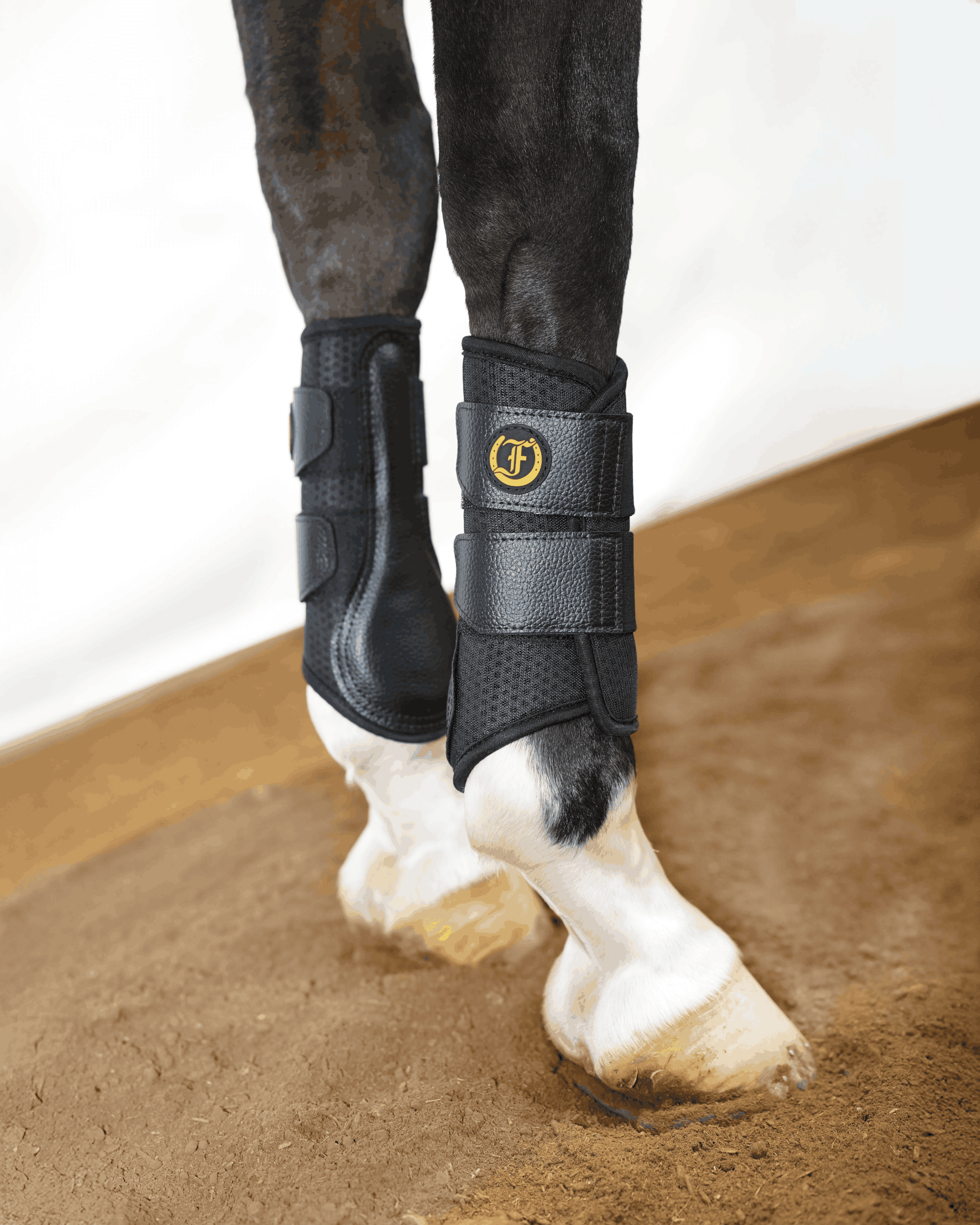 Black protective horse boots with secure straps worn on front legs for training support and leg protection.
