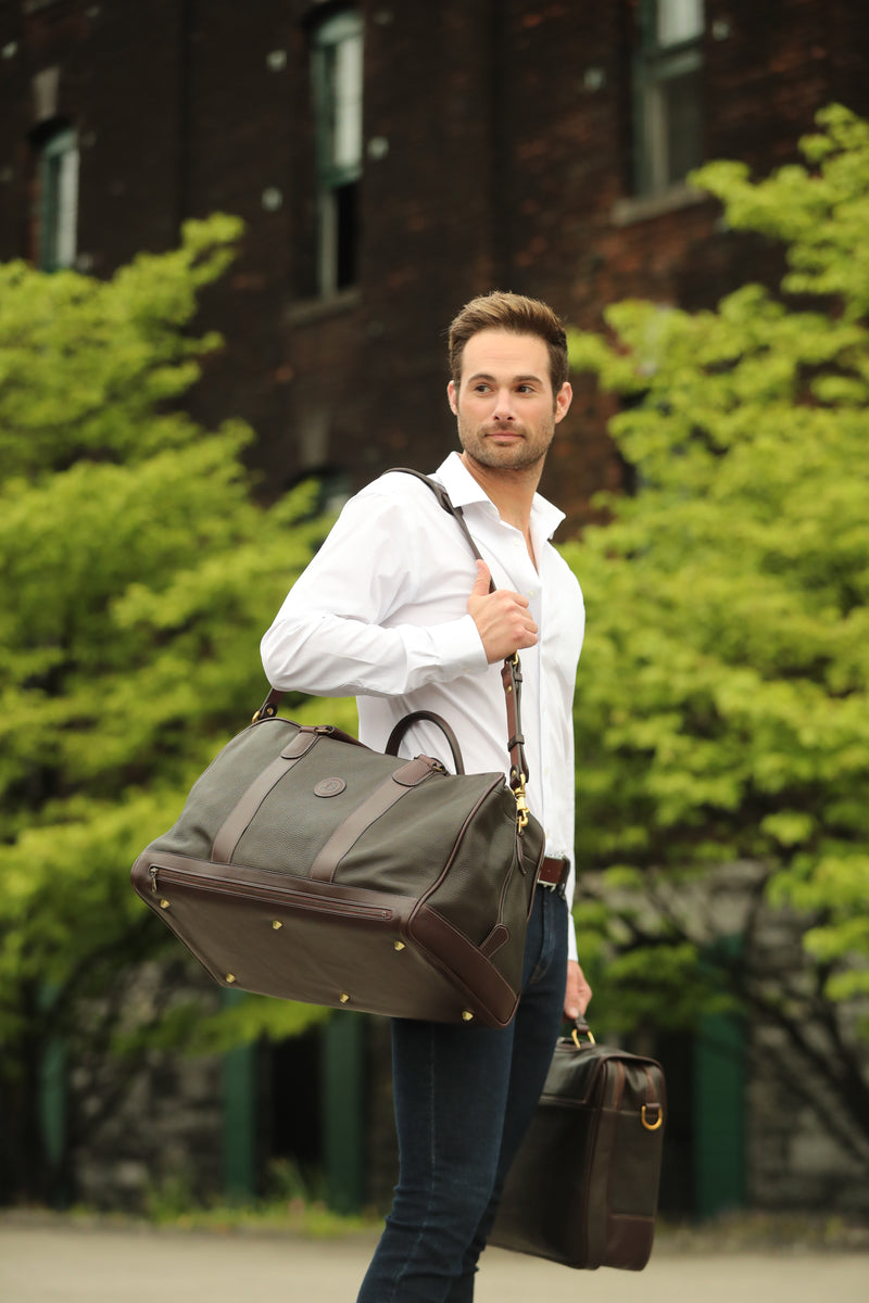 Man carrying The Grand Break travel bag by Freedman’s, a premium leather duffel with brass hardware, exuding style and sophistication.