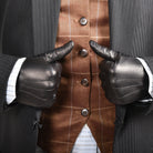 The Yorkville Show Glove, Black leather, worn on both hands with thumbs up gesture, dark suit jacket with striped vest and shirt visible, light background.