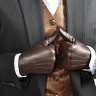 The Yorkville Show Glove, dark brown leather, worn on both hands with thumbs up gesture, dark suit jacket with striped vest and shirt visible, light background.