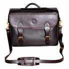Wagonette Briefcase, dark brown textured leather, flap closure with dual buckle straps, silver hardware, contrast stitching, embossed circular logo on front, detachable shoulder strap with padded section, white background.