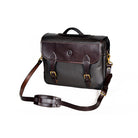 Wagonette Briefcase, dark brown textured leather, flap closure with dual buckle straps, silver hardware, contrast stitching, embossed circular logo on front, detachable shoulder strap with padded section, white background.