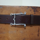 Silver bit buckle detail on brown leather belt, Weymouth model, shown on textured surface.