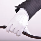 White leather show glove, The Yorkville model, worn on hand holding a riding rein, with jacket sleeve visible.