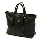 Freedman's Victoria Tote Large, dark textured leather, black leather trim along edges and center straps, embossed circular logo on front, light contrast stitching, dual rolled handles with metal hardware, light background.
